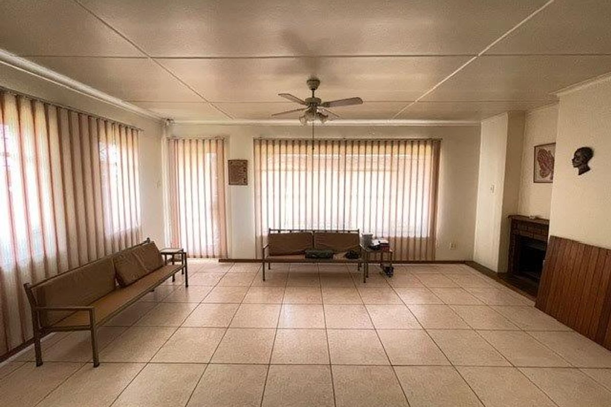Spacious living room featuring large windows with vertical blinds, tiled flooring, a ceiling fan, and a built-in fireplace.