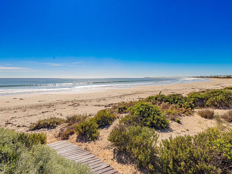 A scenic view of the coastline featuring a wooden boardwalk leading towards the sandy beach and ocean.