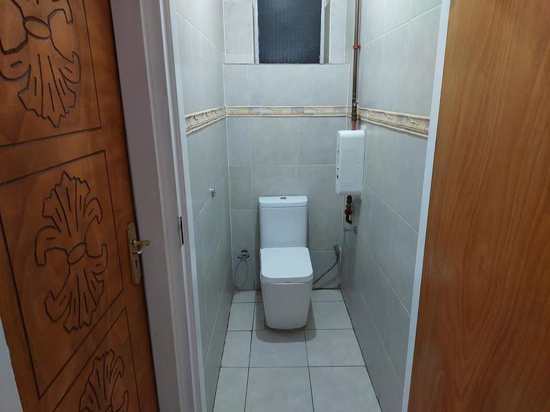 A compact bathroom featuring floor-to-ceiling wall tiles, a modern white toilet, and an integrated water heater unit.