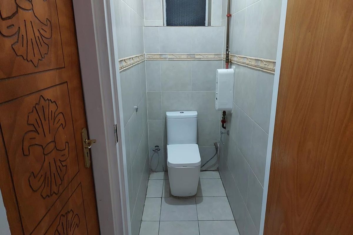 A compact bathroom featuring floor-to-ceiling wall tiles, a modern white toilet, and an integrated water heater unit.