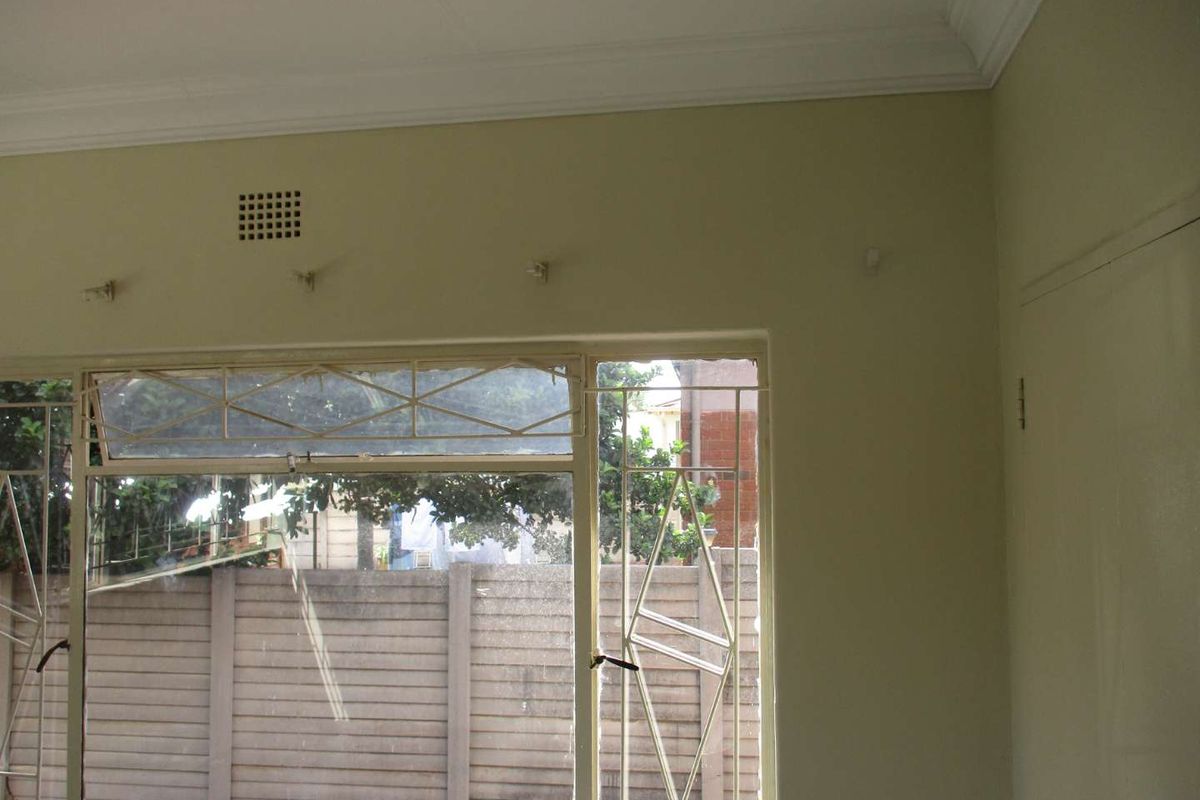 An interior view of a room featuring large windows with security bars, crown molding, and visible wall imperfections requiring maintenance.