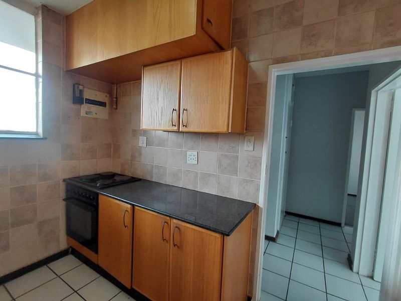 A functional kitchen featuring wooden cabinetry, a built-in oven with hob, and tiled finishes throughout, offering a clean space ready for modernization.