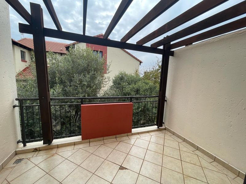 A covered balcony featuring a wooden pergola, tiled flooring, and a metal balustrade, offering an outdoor space for relaxation.