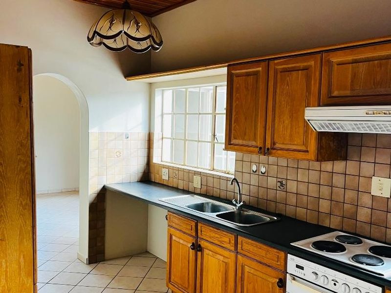 A functional kitchen featuring timber ceilings, wooden cabinetry, tiled backsplash, and built-in appliances, leading through an archway to an adjacent living space.