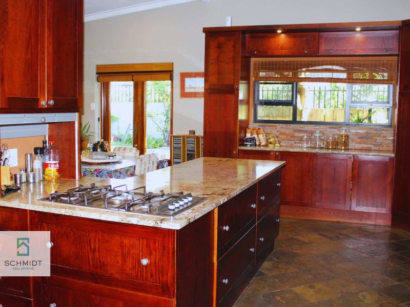 Spacious kitchen featuring rich wooden cabinetry, granite countertops, a central island with a gas hob, and durable stone tile flooring.