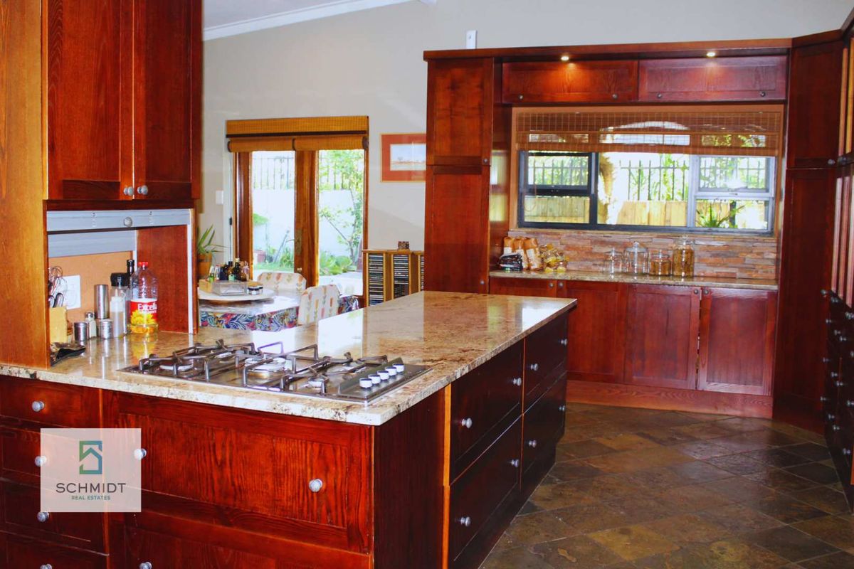Spacious kitchen featuring rich wooden cabinetry, granite countertops, a central island with a gas hob, and durable stone tile flooring.