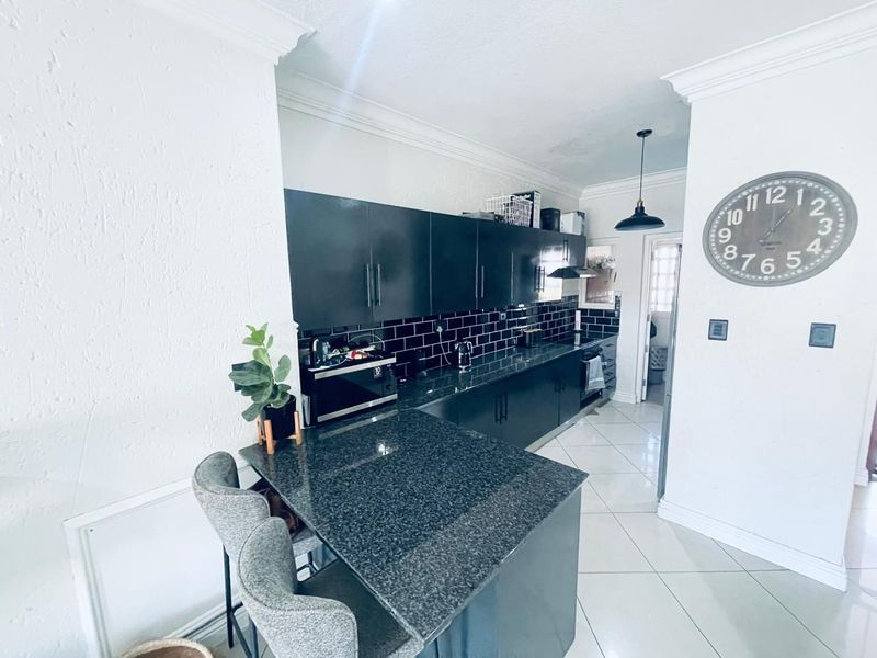Modern kitchen featuring dark cabinetry, granite countertops, a breakfast bar, and a stylish black subway tile backsplash with crown molding details.