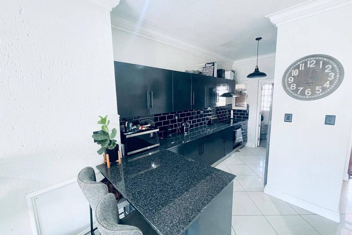 Modern kitchen featuring dark cabinetry, granite countertops, a breakfast bar, and a stylish black subway tile backsplash with crown molding details.