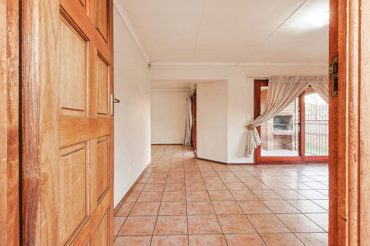An empty living area featuring tiled flooring and sliding glass doors that open to an outdoor patio with a built-in brick braai.