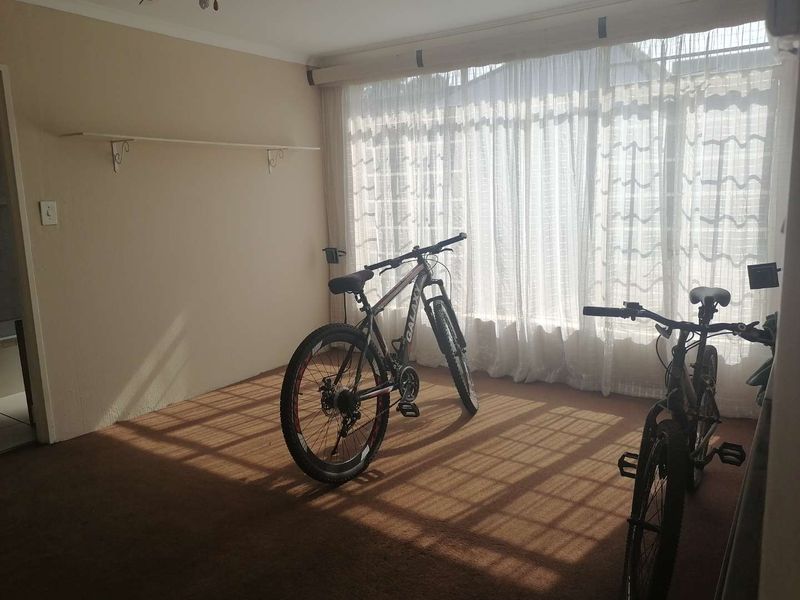 A sunlit living area featuring carpeted flooring and a large window with curtain tracks, offering a blank canvas for interior design.