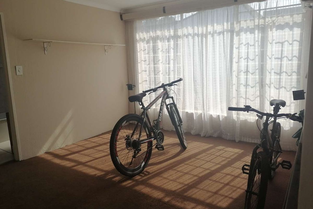 A sunlit living area featuring carpeted flooring and a large window with curtain tracks, offering a blank canvas for interior design.