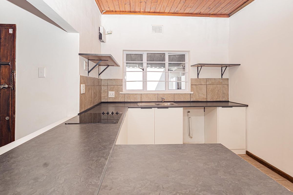 A functional kitchen featuring dark laminate countertops, a built-in hob, stainless steel sink, and timber ceiling, offering a clean and practical workspace.