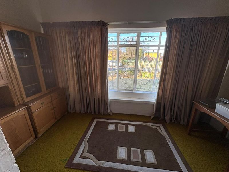 A living room featuring a large window with security bars and carpet flooring, offering a view of the exterior garden area.