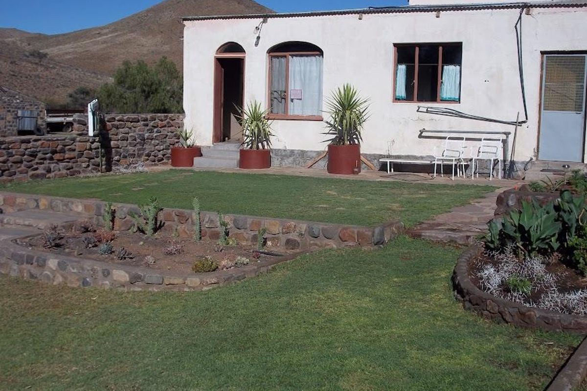 A rear view of the farmhouse featuring a landscaped garden with stone-walled flower beds, a lawn, and direct access to the dwelling.