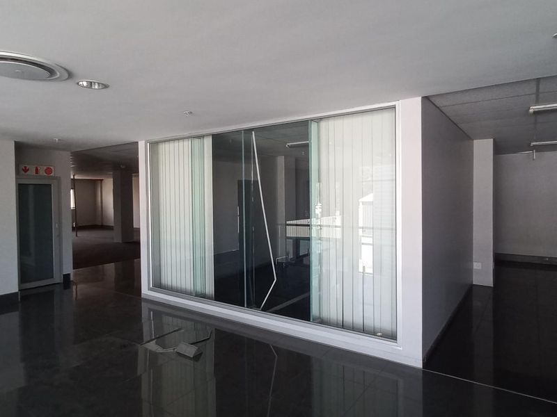 Spacious open-plan office area featuring polished tile flooring, glass partitioning, and recessed lighting, offering a versatile layout for professional use.
