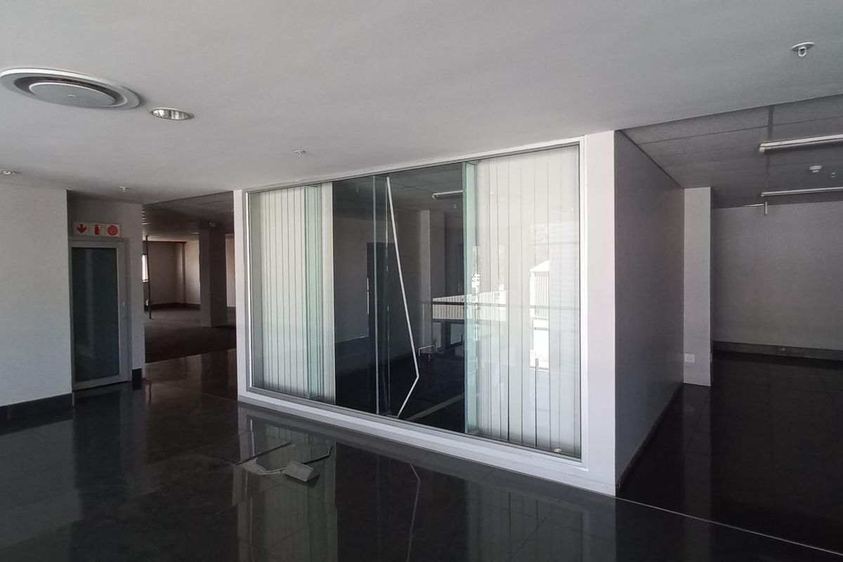 Spacious open-plan office area featuring polished tile flooring, glass partitioning, and recessed lighting, offering a versatile layout for professional use.