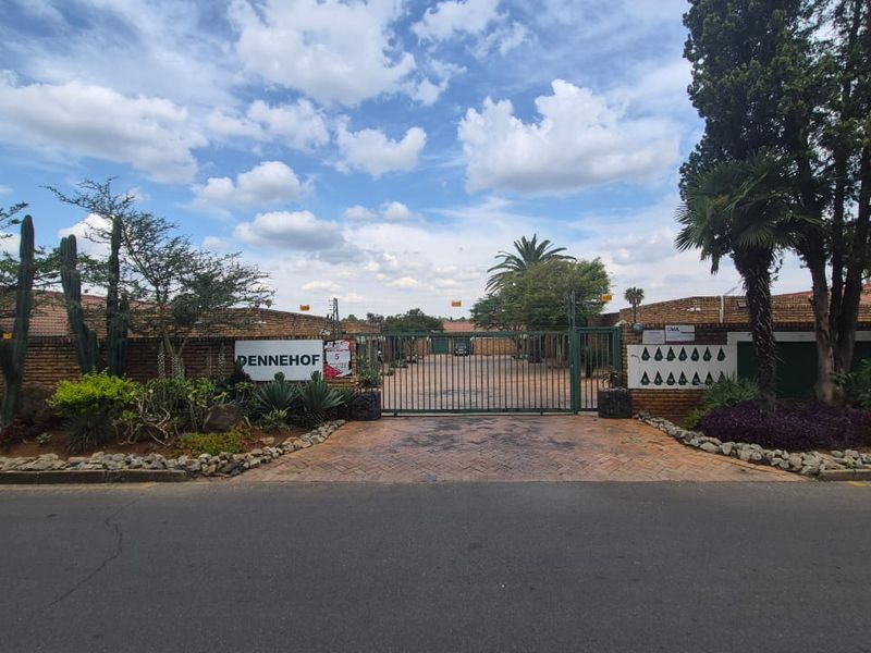 Front entrance view of the Pennehof townhouse complex, featuring a secure gated access point, brick boundary walls, and established garden landscaping.