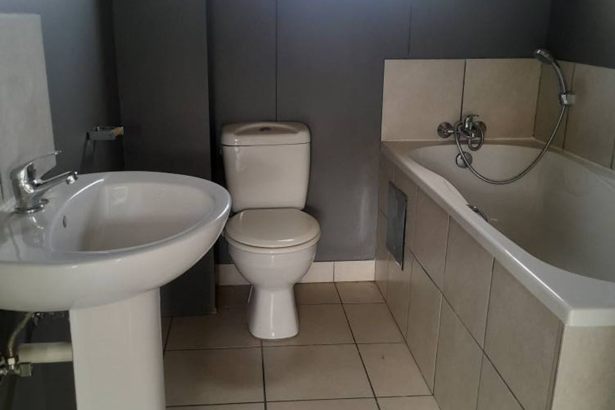 A functional bathroom featuring a pedestal basin, a standard toilet, and a tiled bathtub with a handheld shower attachment.
