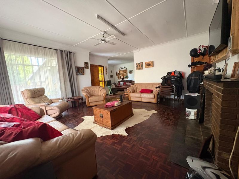 Spacious living room featuring classic parquet flooring, a brick fireplace, and a ceiling fan, offering a comfortable and traditional living space.