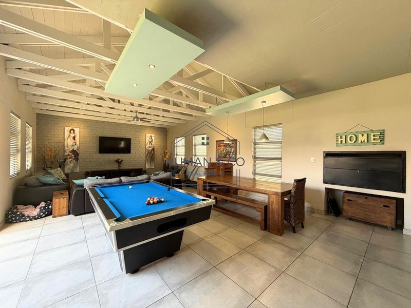 Spacious open-plan living area featuring exposed roof trusses, tiled flooring, a brick feature wall, and a built-in fireplace.