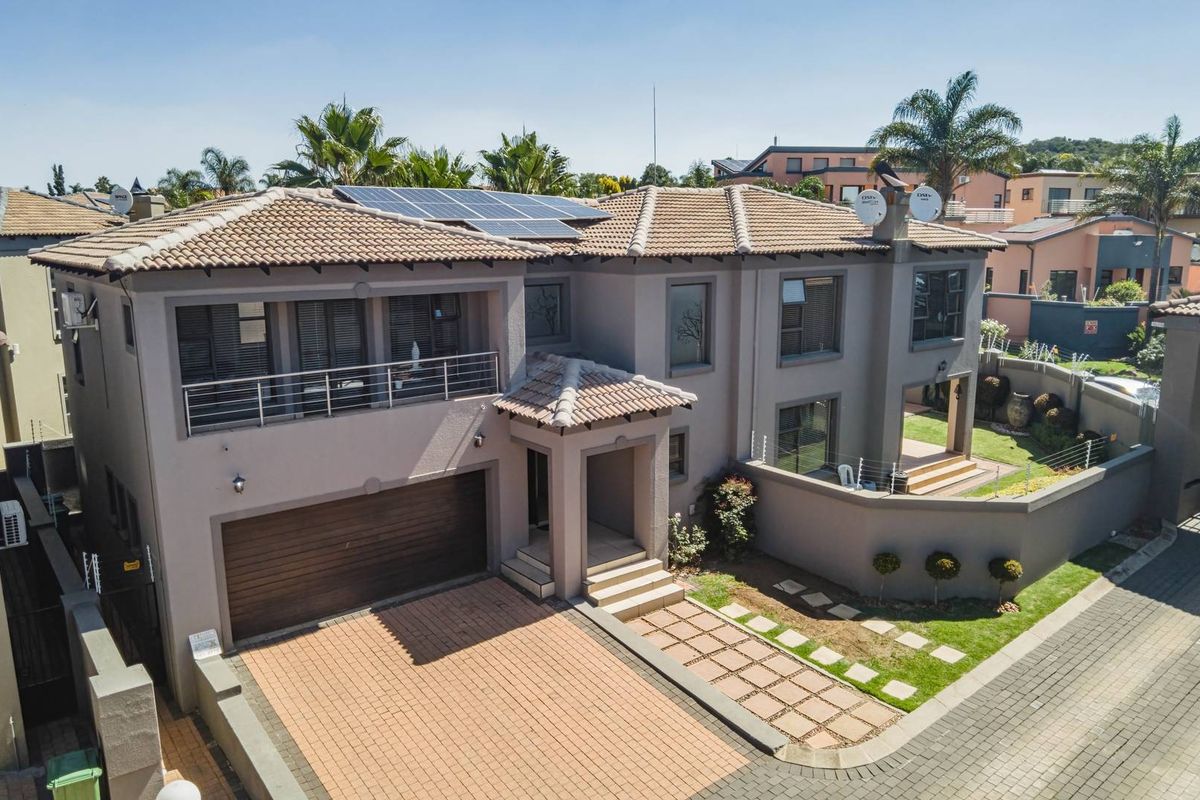 Aerial view of a modern double-story residential property featuring a tiled roof, solar panels, paved driveway, double garage, and a balcony.