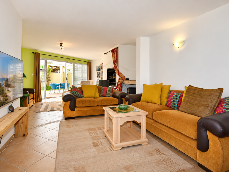Spacious open-plan living area featuring tiled floors, wall sconce lighting, and large sliding glass doors providing seamless access to the outdoor patio.