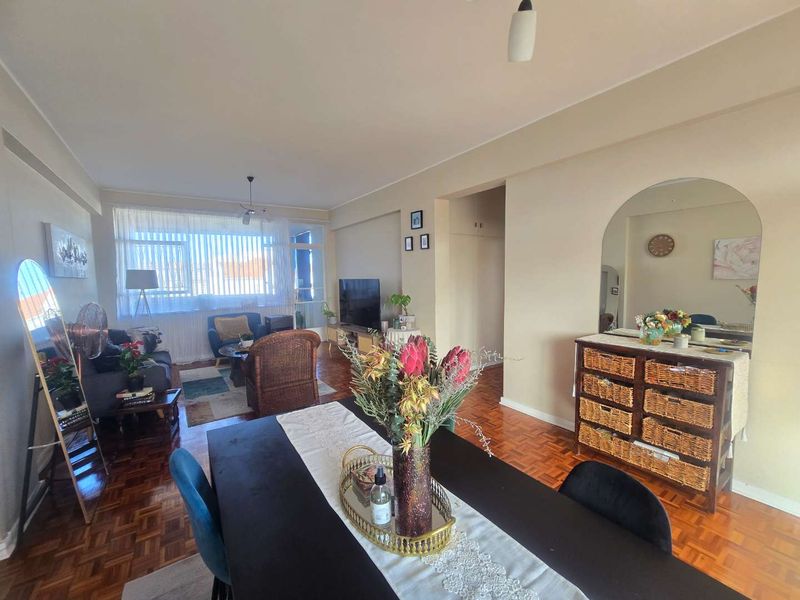 Spacious open-plan living and dining area featuring classic parquet flooring and natural light through large sliding glass doors.