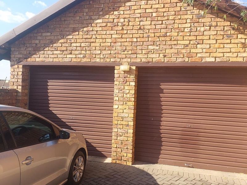 A double garage with brown roller doors and a face brick exterior, featuring a paved driveway approach.