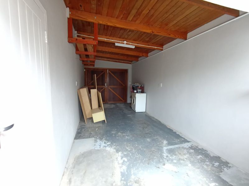 A functional garage space featuring exposed timber ceiling beams, double timber doors, and a concrete floor, offering potential for storage or workshop use.