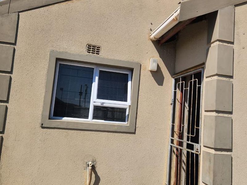 Front exterior view of the property featuring a security gate, paved entrance area, and wall-mounted satellite dish.