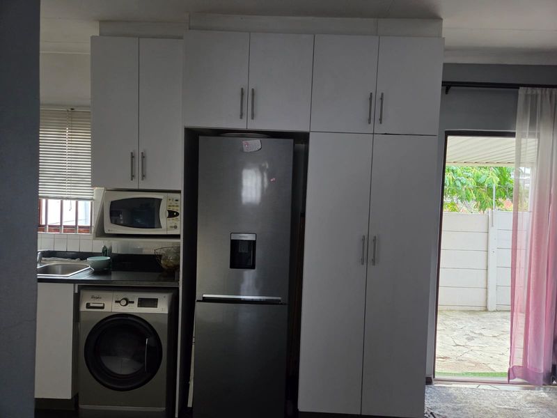 A functional kitchen area featuring white built-in cabinetry, granite countertops, a stainless steel sink, and a tiled backsplash with direct access to the outdoor patio.