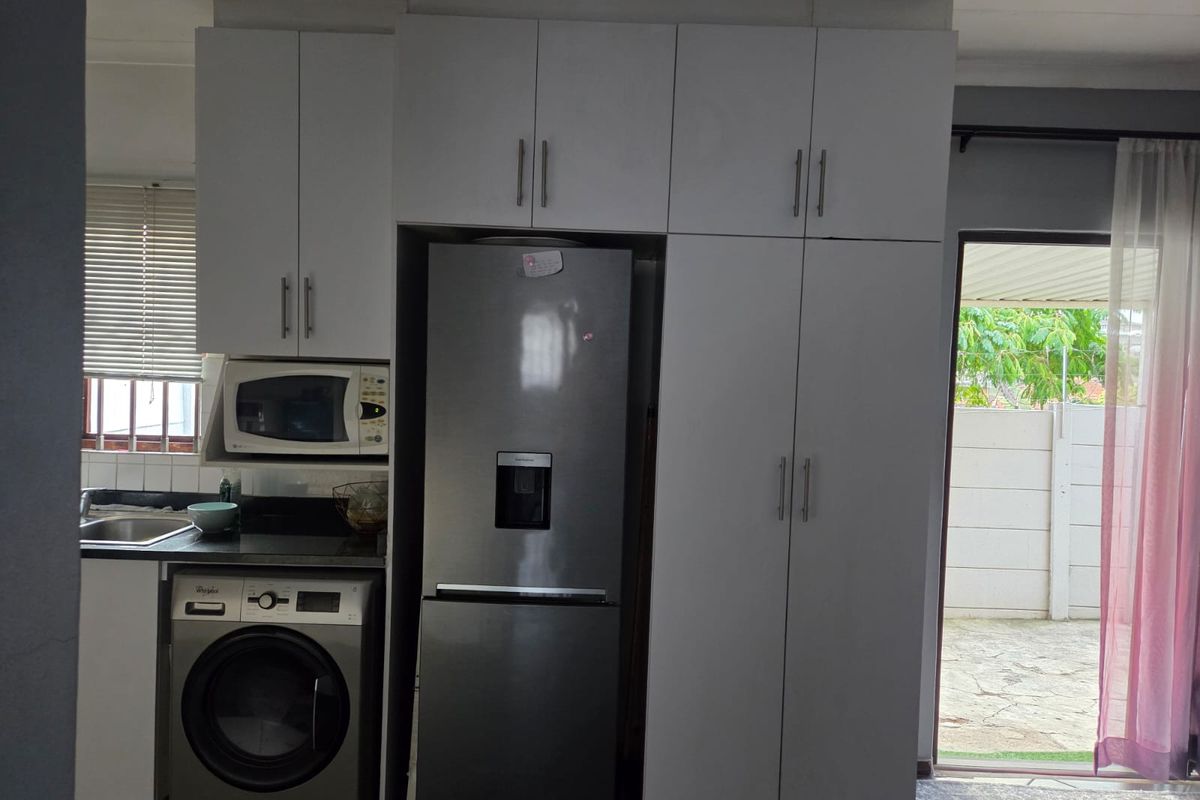 A functional kitchen area featuring white built-in cabinetry, granite countertops, a stainless steel sink, and a tiled backsplash with direct access to the outdoor patio.