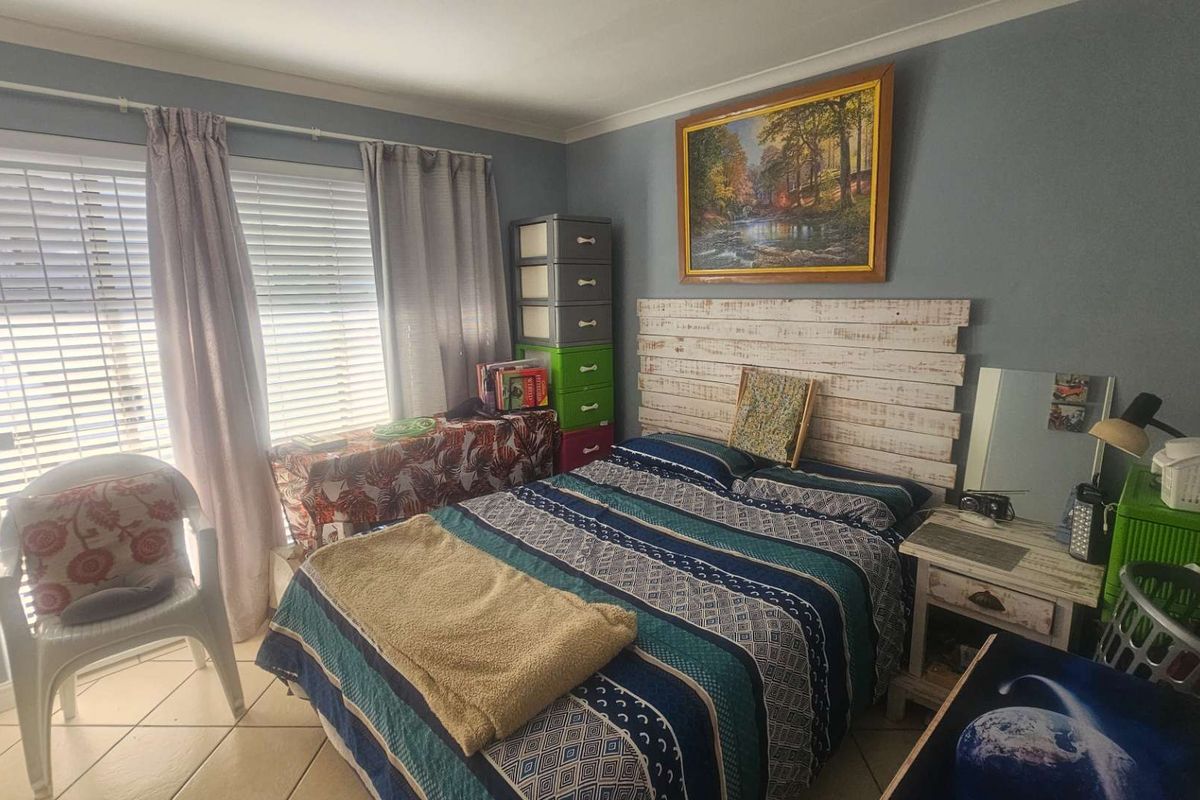 A bedroom featuring tiled flooring, large windows with blinds, and neutral wall paint, providing a functional living space.