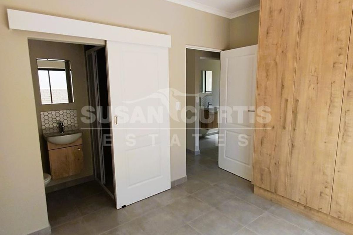 A modern bedroom featuring neutral tiled flooring, built-in wooden cabinetry, and an en-suite bathroom with a sliding door entrance.