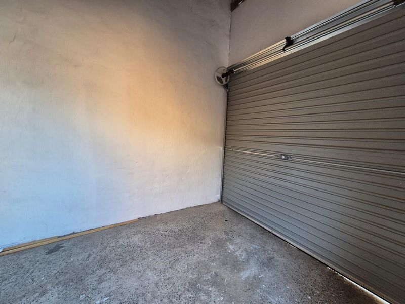 A functional garage space featuring a standard roller door and exposed concrete flooring, providing secure vehicle storage or utility space.