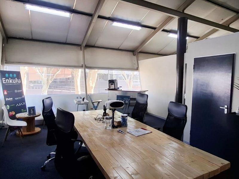 A functional office space featuring exposed steel roof trusses, large windows providing natural light, and carpeted flooring in a professional business setting.