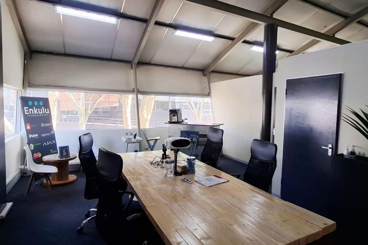 A functional office space featuring exposed steel roof trusses, large windows providing natural light, and carpeted flooring in a professional business setting.