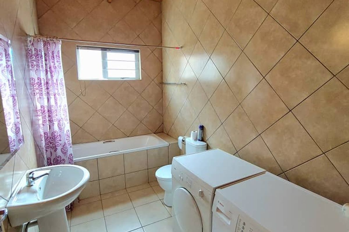A functional bathroom featuring a bathtub, pedestal basin, and integrated laundry space with tiled walls and a timber-paneled ceiling.