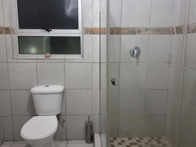 A functional bathroom featuring a glass-enclosed shower, tiled walls, and a standard toilet, providing a clean and practical space.
