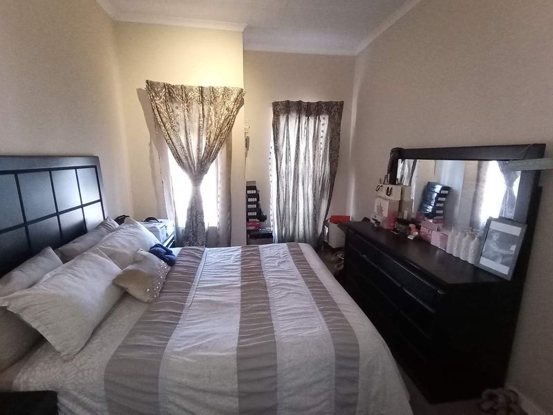 A standard bedroom featuring neutral wall finishes, coving, and dual window access with existing curtain fixtures.