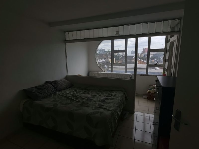 Bedroom featuring a unique circular window design and an internal partition wall, offering natural light and views of the surrounding urban area.
