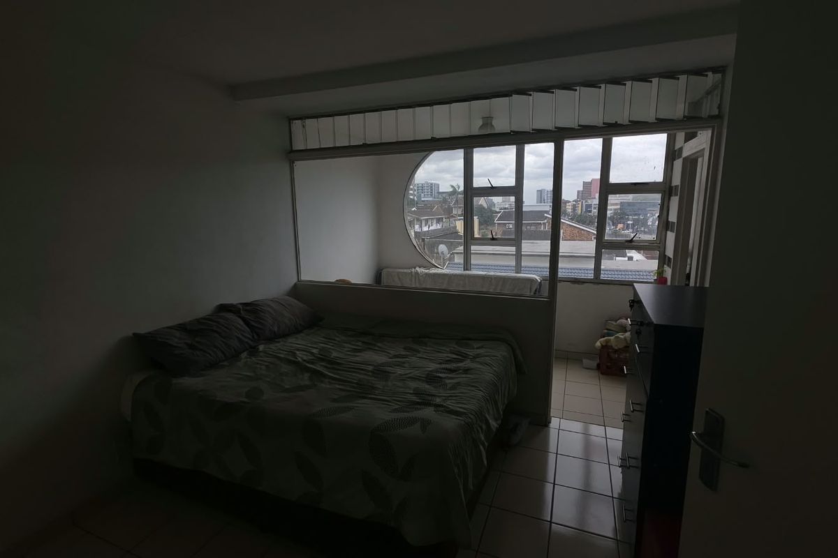 Bedroom featuring a unique circular window design and an internal partition wall, offering natural light and views of the surrounding urban area.
