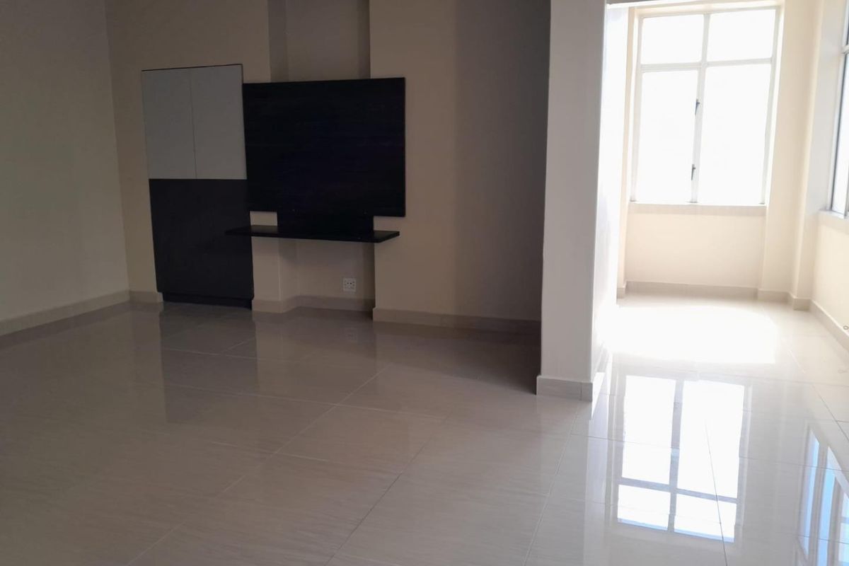 A bright, empty living room featuring polished tiled flooring, a built-in media console, and large windows allowing for ample natural light.