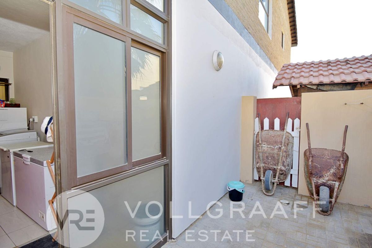 A paved rear courtyard area featuring a sliding door entrance and boundary wall with exterior lighting.