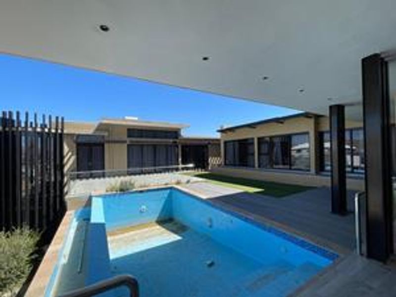 Outdoor entertainment area featuring a covered patio with recessed lighting and an empty swimming pool with decking.