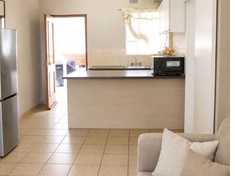 Open plan living area featuring tiled floors and a functional kitchen with built-in cabinetry and counter space, leading to an exterior entrance.
