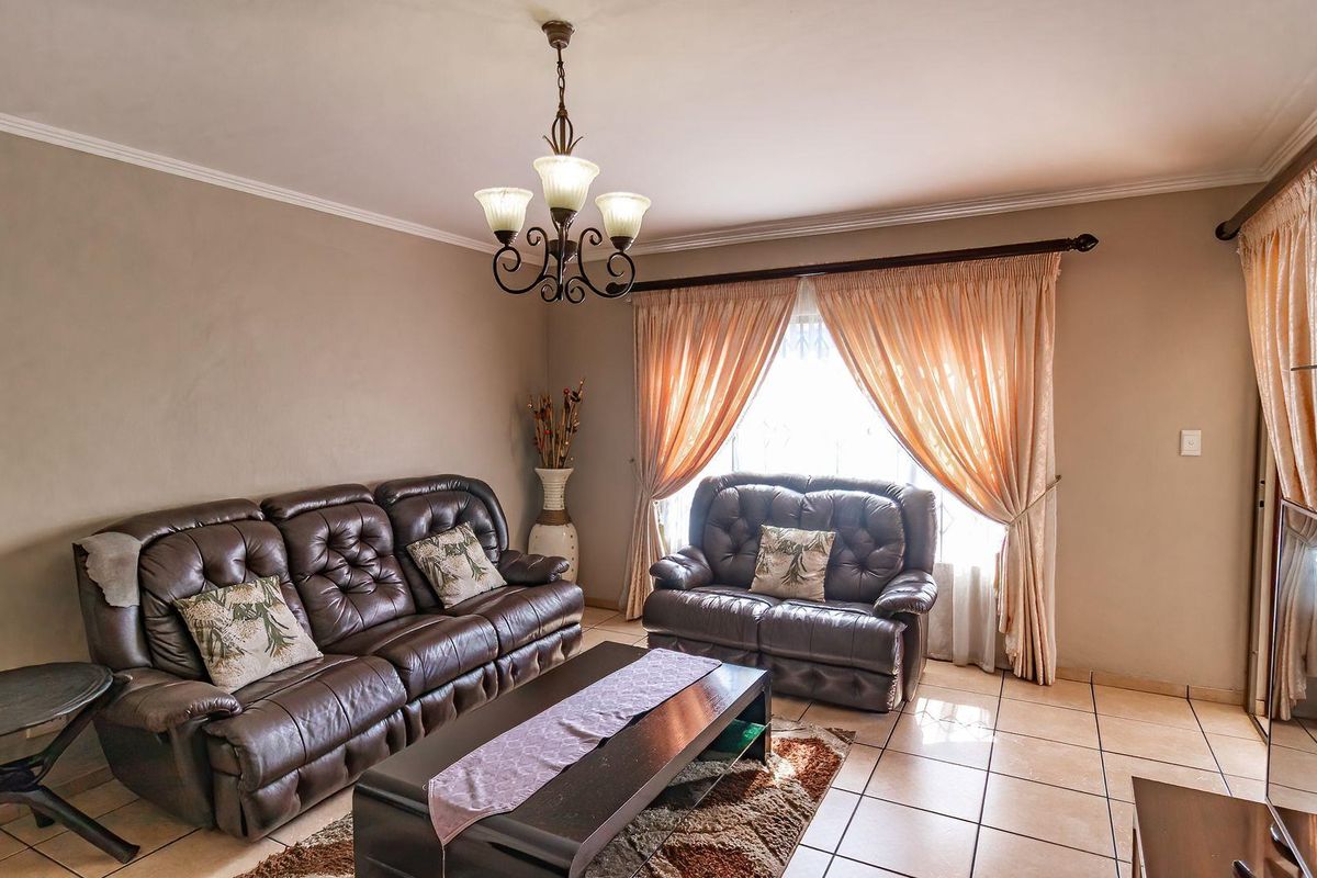 A comfortable living room featuring tiled flooring, a decorative chandelier, and large windows with curtain treatments, providing a functional and inviting space.