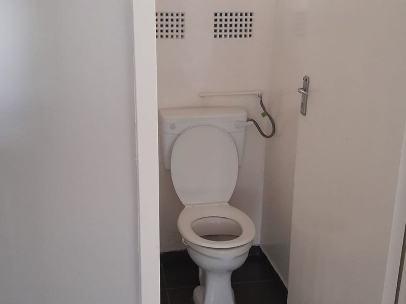 A small, functional bathroom featuring a standard toilet and wall-mounted ventilation grilles, requiring minor cosmetic updates to the exposed plumbing.