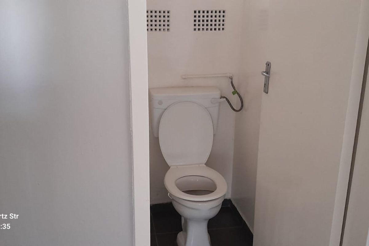 A small, functional bathroom featuring a standard toilet and wall-mounted ventilation grilles, requiring minor cosmetic updates to the exposed plumbing.