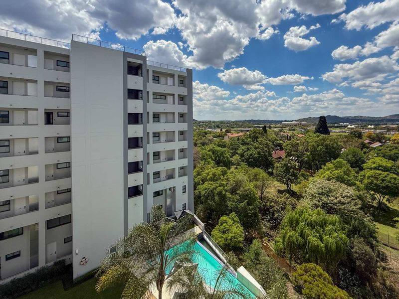 Aerial view of a modern multi-story apartment complex featuring a swimming pool and surrounding lush green landscape.